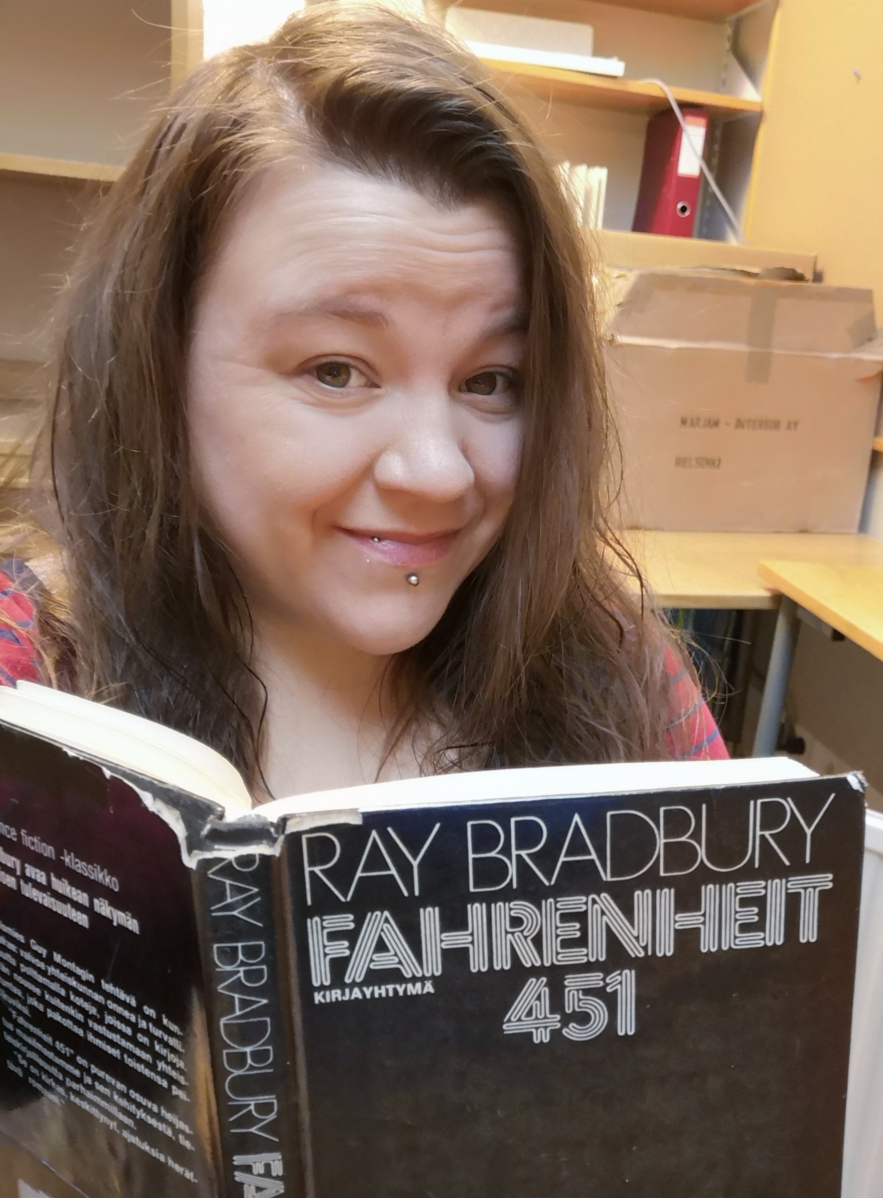 Ruskeatukkainen nainen hymyilee kameralle edessään avoin kirja. Kirjan kannessa lukee "Ray Bradbury Fahrenheit 451".