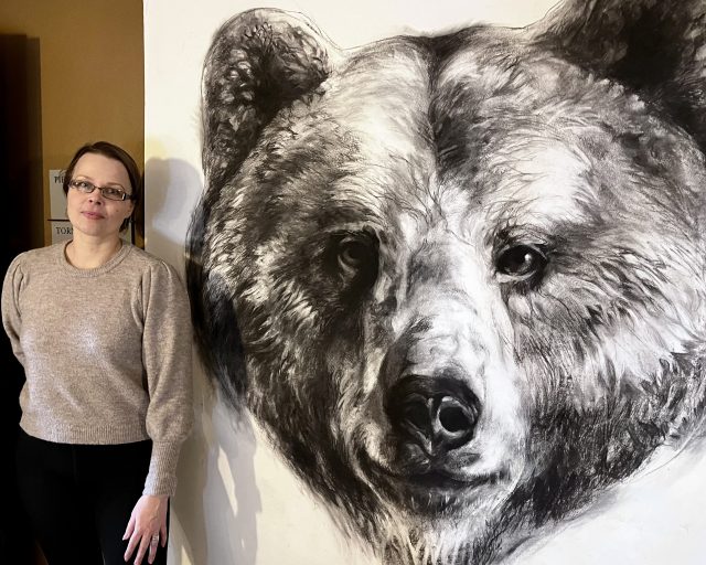 Kuvataiteilija Sanni_Maaria Puustinen seisoo suuren karhua esittävän hiilipiirroksen edessä.